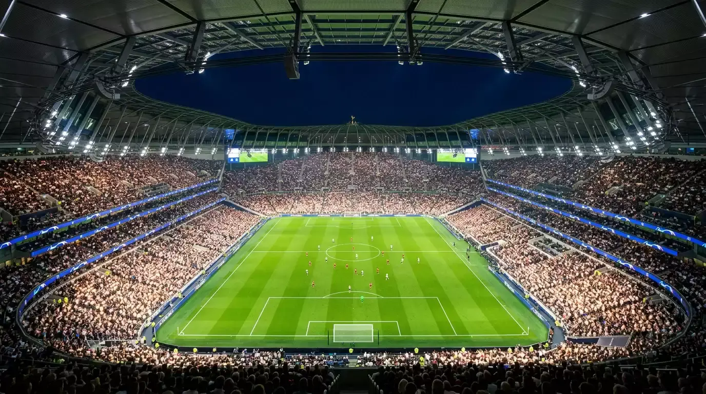 Estadio de futbol iluminado durante un partido nocturno de Champions League con cesped verde y gradas llenas