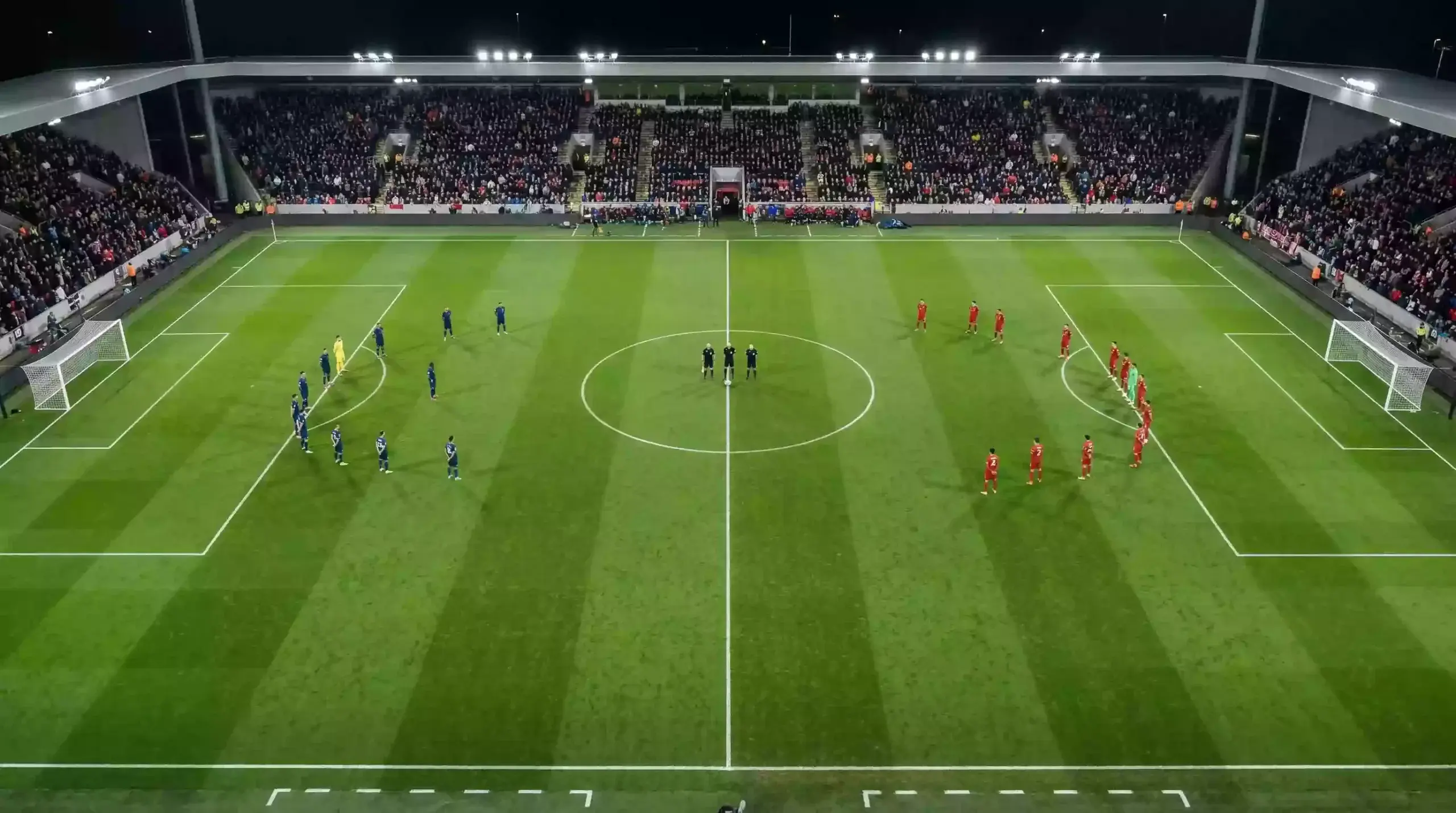 Campo de fútbol con líneas de juego marcadas y dos equipos posicionados antes del saque inicial en un partido nocturno de Champions League